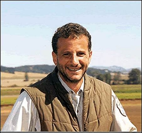 A portrait of Richard Guadagno in a U.S. Fish and Wildlife Service uniform with a field and mountains in the background