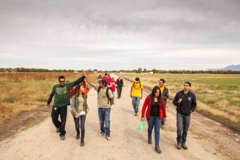 A group of 13 youth and staff members walk down a dirt and gravel road with a field on their side