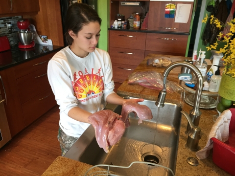 A young woman in a kitchen holds meat from a wild turkey over a sink