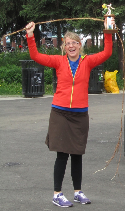 Smiling woman holding above her head a long root in one hand and a trophy in another