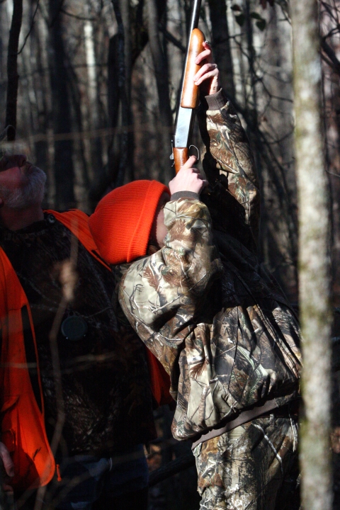 A youth hunter pointing a gun up in a tree.