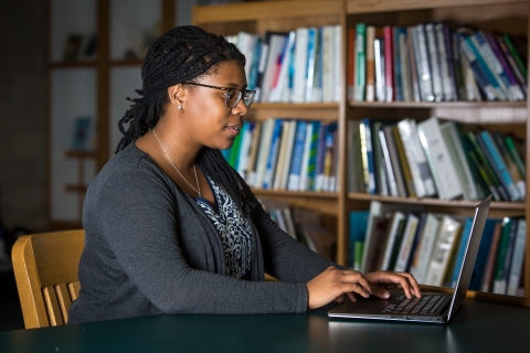 Liberian working on laptop with bookshelf in background