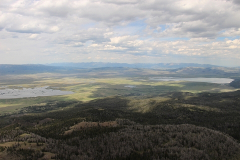 View of nearly the entire Refuge as seen from atop the summit of Baldy Mountain at 9863 feet; view includes Upper and Lower Lake, conifer forest, and a green valley floor with both lakes, wetlands and partly cloudy skies