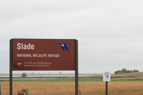 Slade National Wildlife Refuge sign in front of a grassy or agricultural field