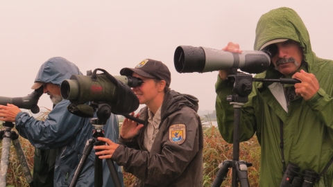 Three people look through spotting scopes.