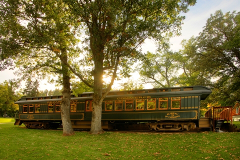 A rail car sits on display surrounded by green grass and trees. The rail car is painted green with gold trim and lettering. The lettering reads "Bureau of Fisheries 3."