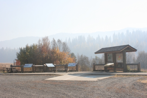 Auto Tour Stop parking area with a shaded kiosk and three interpretive panels in front of a pine forest. 
