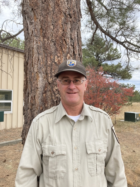 A man in Fish and Wildlife Service Uniform standing outside next to a tree