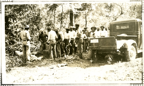 Black and white photo of around 20 African American men in a line in the woods.