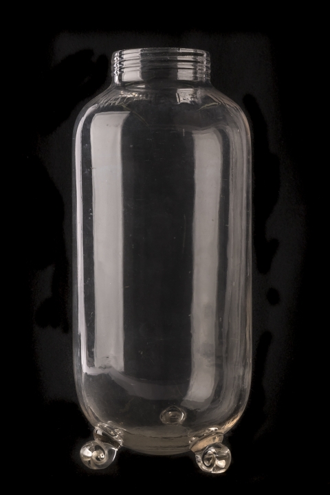 A large clear glass jar with swirled glass feet and a rimed top sits atop a black background.