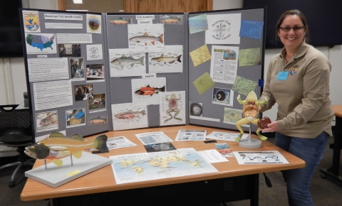 Photo of Lacey Hopper holding dissecting frog demo at Bozeman Fish Health Center outreach table
