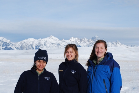 Three winter naturalists smiling in a snowy field.