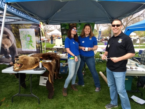 Three FWS employees at an environmental fair. There is a bear hide on a table in the left side of the frame