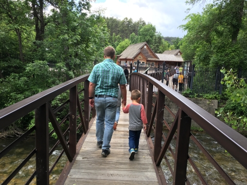 A father holds his young sons hand as they walk across the a bridge over a fast running creek that leads into the fish hatchery grounds.