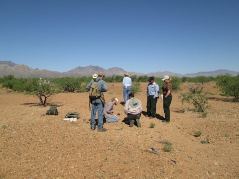a group of seven people are in the desert with mountains and sparse vegetation in the background
