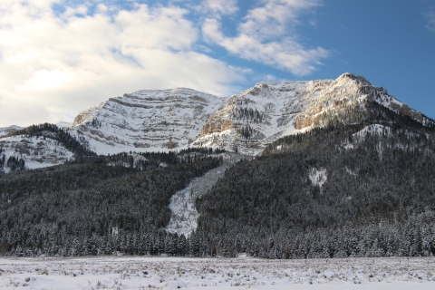 Sun shines through the clouds on the snowy rock face of a mountain.