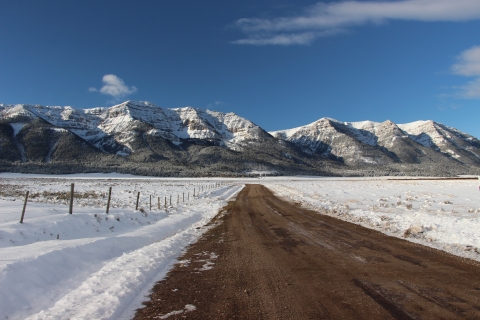 Brilliant blue skies prevail during a winter day with a snow covered landscape and Centennial Mountain Range in the background as seen from a roadway