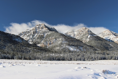A view of snowy mountains in winter with clouds forming on a sky blue day