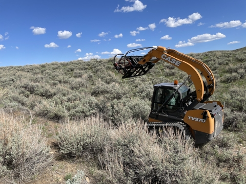 A piece of small equipment can be seen in a sagebrush landscape working to remove fence.