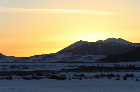 A bright yellowish winter sunrise about to crest the mountains and spill onto a snowy Refuge valley floor.