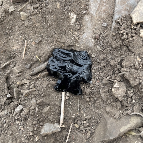A broken obsidian arrow point sitting in dirt