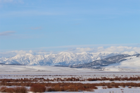Snow covered mountain range as seen from across a snow covered valley is shown.
