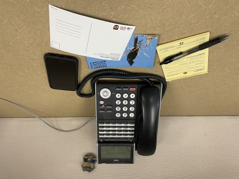 Photo of a phone, mobile phone, two postcards, and a yellow notepad