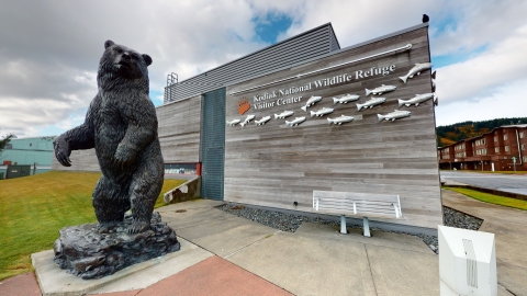 statue of a bear in front of a building with metal salmon on it reading kodiak national wildlife refuge visitor center