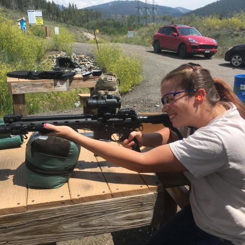 A woman sighting a gun on a wooden table
