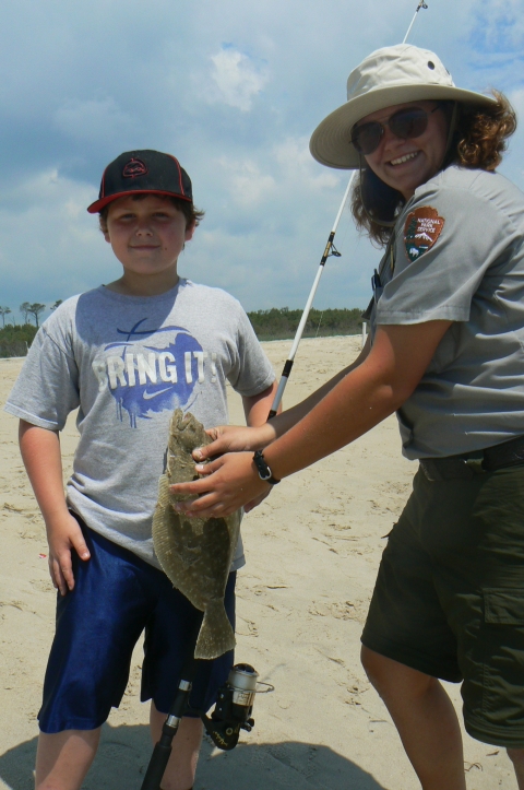 A National Park Service ranger poses with a child and a fresh caught flounder fish