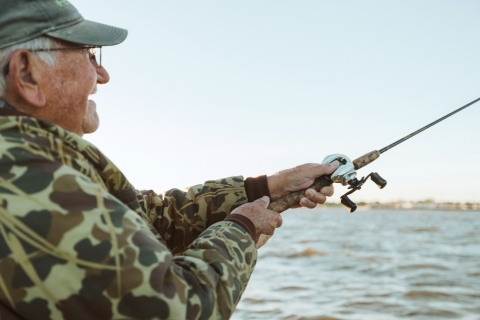 An older man enjoys fishing at the water's edge. 