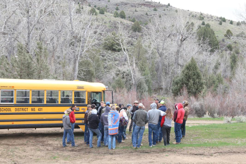 A group of students stand around a school bus in an undeveloped landscape