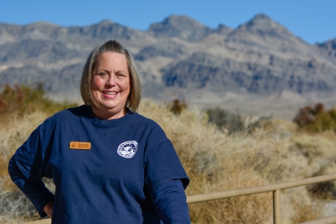 Woman in a blue shirt smiling. Mountains in the distance. 