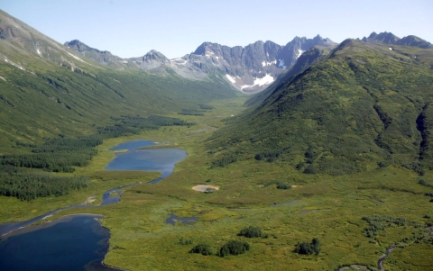 Two small deep blue lakes in a steep, verdant valley with snow-capped mountains in the distance