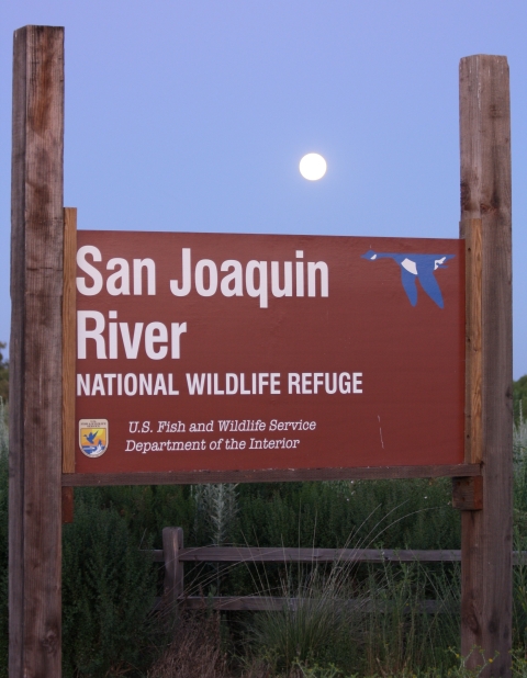 Brown sign for "San Joaquin River National Wildlife Refuge" with background of moon rising in the sky.
