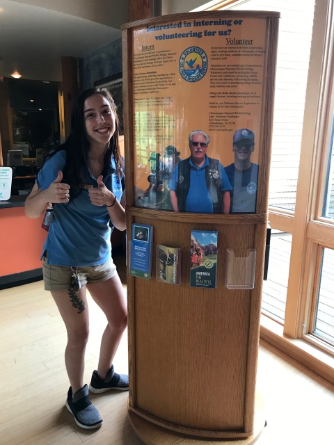 An intern gives two thumbs up next to a volunteer recruitment poster