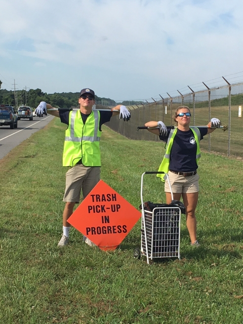 Two volunteers posing behind a "trash pick-up in progress" sign.