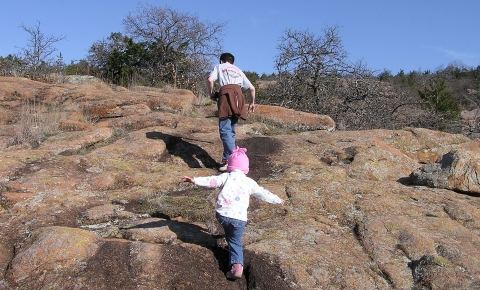 A young children following an adult up a wide, rocky trail
