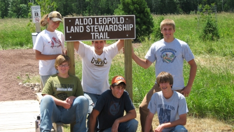 Young YCC workers posing next to Aldo Leopold Land Stewardship Trail sign