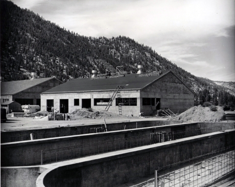 Black and white photo of a concrete building under construction in the background, and oval concrete ponds in the foreground.