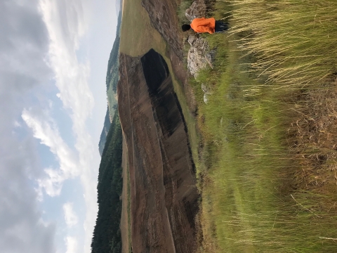 A person in an orange jacket stands at the edge of an open pit mine