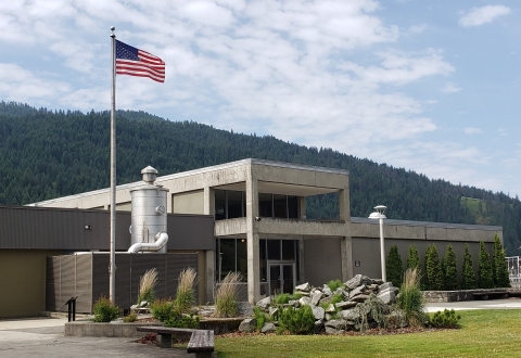 The front of Dworshak National fish hatchery main administration building. In the forefront a natural-looking water feature is shown with an American Flag on a flagpole.