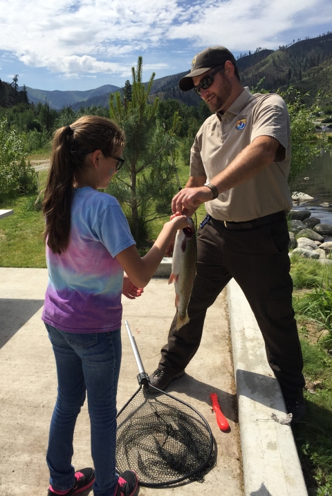 A man in Service uniform hands a girl in a rainbow tie-dye shirt her trout.