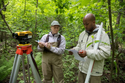 man and woman with survey equipment with woods in background