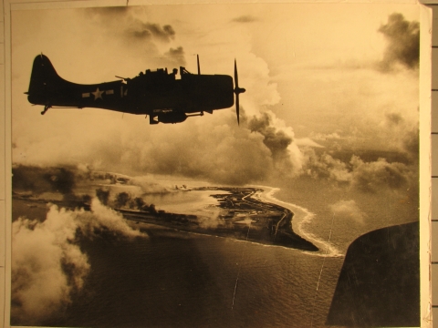 A World War 2 plane flies above Wake Atoll. The image is black and white, but an orange hue covers the image.