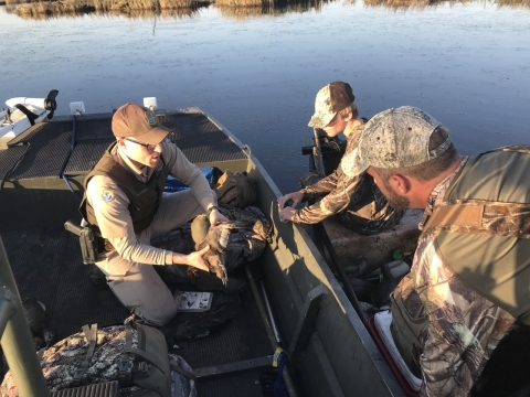 An image of a Federal Wildlife Officer on a boat checking a hunter's harvest.