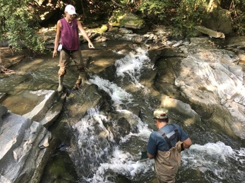 Two community members stand along a small waterfall in a creek