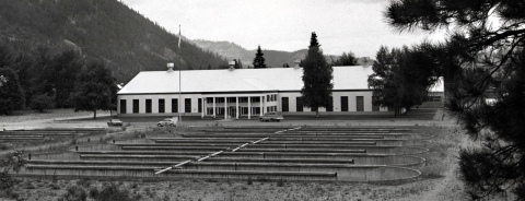 Black and white photo looking over large oval fish ponds to a long building with tall windows.