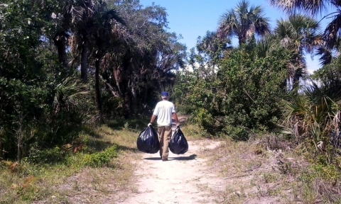 A volunteer carrying trash bags off a trail.