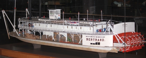 A model of a white 18th-century steamboat with red paddlewheels